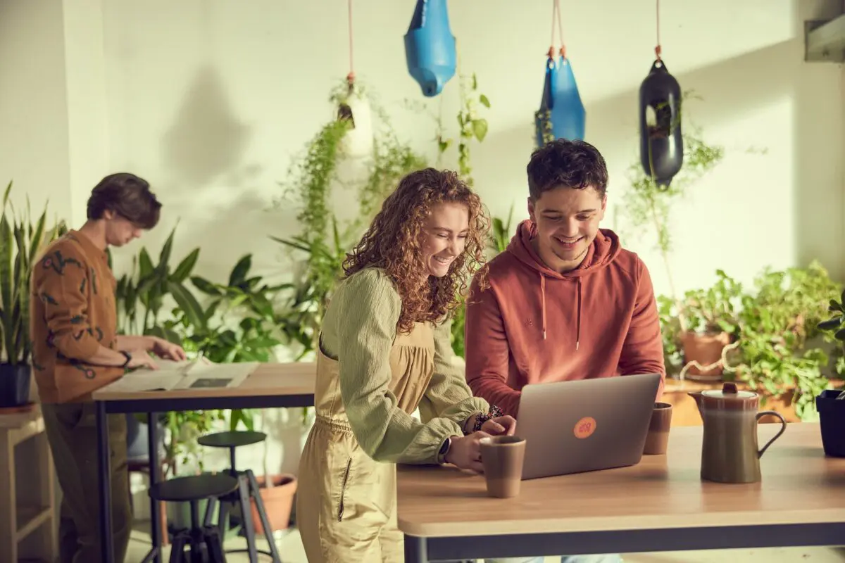 Jongen en meisje werken samen in een lichte en groene omgeving op de laptop.