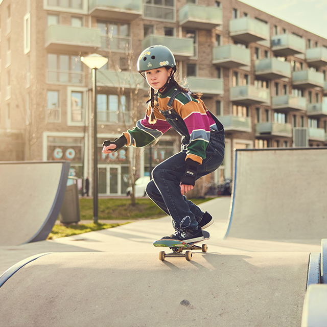 Kind op een skatebord in een skatepark met een flat op de achtergrond